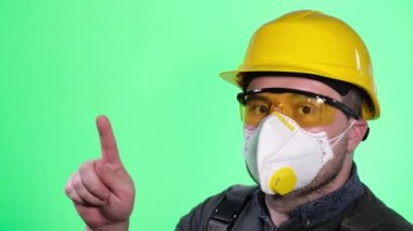 Yeşil ekran arkaplanındaki kameraya bakan koruyucu maskeli bir inşaat işçisinin portresi..