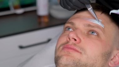 Kaplıcada yüz bakımı yaptıran genç bir adam. Bir insanın yüzünde kil maske. Bir kozmetolog yüzüne nemlendirici bir maske takarak yüz masajı yapar.
