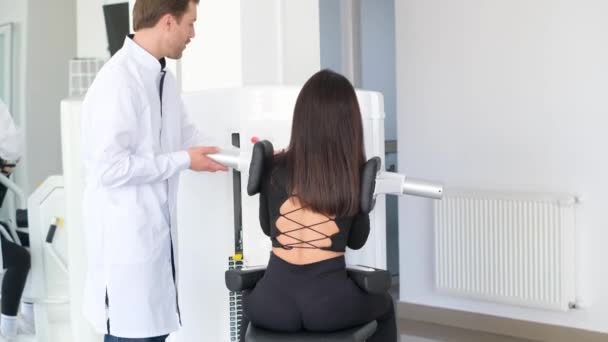 一位年轻妇女正在与理疗师一起在一台诊断机器上做脊柱检查 骨质疏松症 椎间盘突出 椎间盘突出症 — 图库视频影像