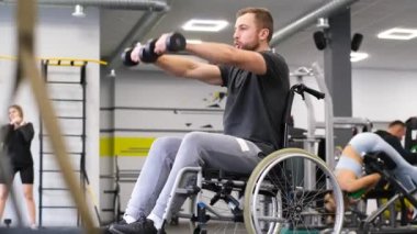 Tekerlekli sandalyedeki engelli bir adam spor salonunda dambılları kaldırıyor. Spor konsepti.