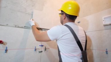 Bir tiler banyodaki bir duvara seramik fayanslar sergiler. Tulum ustası duvara seramik fayanslar koyar..