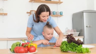 Güzel anne ve oğul evde yemek pişirirken sebze doğruyor ve gülümsüyor. Anne oğluna salata yapmayı öğretiyor..