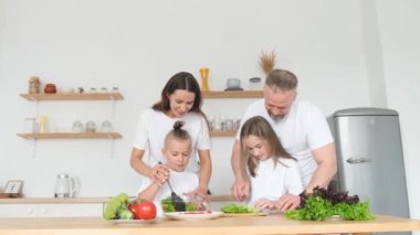 İki küçük çocuklu mutlu bir aile mutfakta birlikte yemek pişiriyor, gülümseyen ebeveynler küçük çocuklara sağlıklı yemek, organik salata ya da akşam yemeği yapmayı öğretiyor..