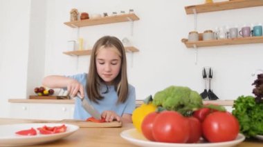 Küçük bir kız taze sebzelerden bir salata hazırlıyor. Dersten önce kahvaltıda. İtaatkar çocuklar