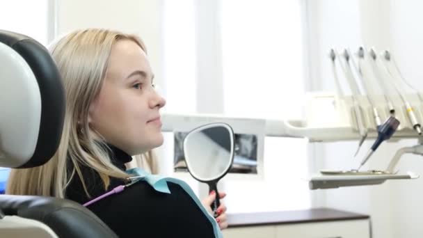 満足した笑顔の女性のクライアントの肖像画は 歯科椅子に座って 鏡の中で彼女の治療歯を見て 歯科治療の結果 口腔の問題のタイムリーな治療 — ストック動画