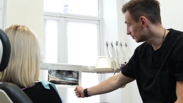 Молодой Дантист Показывает Рентген Зубов Привлекательному Клиенту Обсуждение Плана Стоматологического — стоковое видео