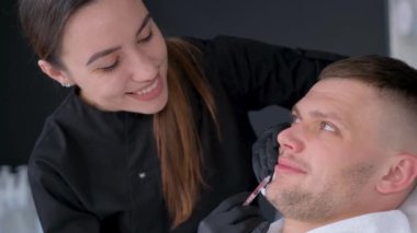 Botoks enjeksiyonu yapan bir kozmetikçiyle randevusu olan tatmin olmuş bir müşteri. Modern genç bir adamın yüz derisinin gençleşmesi.