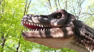 Korkunç bir dinozorun kafasının, orman ve gökyüzünün arka planına karşı büyük dişleri olan görüntüsünü yakınlaştır. Dinozorların modern modelleri