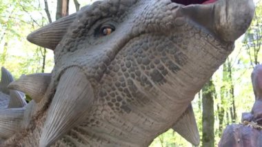 Korkunç bir dinozor avcısının kafasının büyütülmüş görüntüsü namlusunu ortaya çıkarıyor. Çocuklar ve yetişkinler için bir lunaparktaki dinozor modelleri. Dinozorların tarihini çalışıyorum..