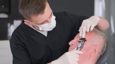 Bir plastik cerrah yaşlı bir adamın gözünün altındaki eski kırışıklıkları inceler. Modern plastik cerrahi kliniği.