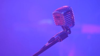 Kapalı alandaki bir karaoke kulübünde çok renkli spot ışıklarıyla şarkı söylemek için bir mikrofonun yakın çekimi. Profesyonel ses kayıt mikrofonu, yakın plan..