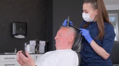Bir trikolog detaylı bir saç teşhisi koyar ve yaşlı bir adamı muayene eder. Saç tedavisi konsepti. Kellik ve saç kaybı. Dikey video
