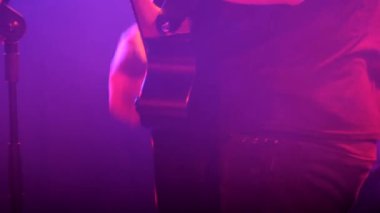 Bir müzisyen sahnede bir konser sırasında akustik gitar çalar. Müziğini vurgulamak için boncuk, ton ve ses kontrolü ve gitar efektörü kullanıyor.