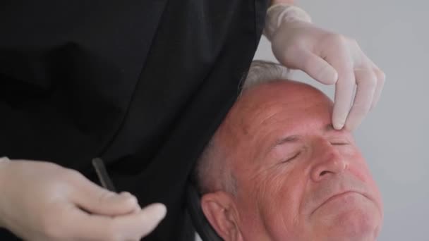 一位特写整形外科医生在一位老年人的眼皮底下检查老旧的皱纹 美国现代整形外科诊所 — 图库视频影像