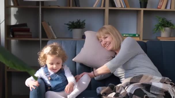 祖母は孫娘を寝かしつける ソファに腰を下ろしていると元気いっぱいの子供が遊んでいる 4Kビデオ — ストック動画