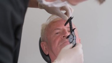 Doktor cerrahın portresi erkek yüzünde iz bırakıyor, yaşlı adam. Dikey video.