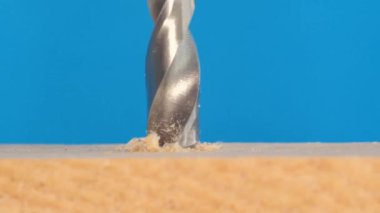 Güzel mavi bir arka planda metal matkapla ahşap bir yüzeye delik açmaya yakın plan. Elektrikli aletlerin makro videosu. Dikey video
