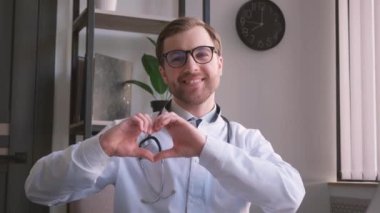 Doktor kameraya bakarak kalp hareketini ve gülüşünü gösterir. İnsanları tedavi etme kavramı. Dikey video
