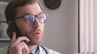 Genç, yakışıklı doktor ofisinde telefonla konuşuyor. Profesyonel bir doktorun tıbbi muayeneleri. Modern tıbbi bakım