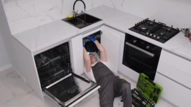 Üniformalı genç tesisatçı mutfak odasında lavabo tamir ediyor. Usta bir muslukçunun evine bir telefon. Dikey video