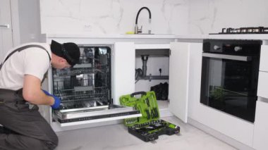 Tamirci Mutfaktaki Alet kutusuyla bulaşıkçıyı inceliyor. Bir adam bulaşık makinesini tornavidayla söker..