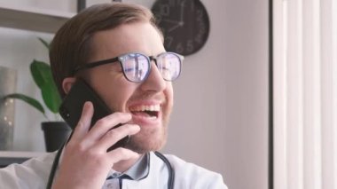 Genç bir erkek doktor ofiste akıllı telefon kullanarak konuşuyor. Mutlu bir doktor iyileşmiş bir hastayla konuşuyor. Yüksek kalite 4k video