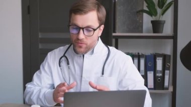 Tecrübeli bir doktor laptopta bir hastaya video danışmanlık yapar, ilaç tavsiye eder ve yazar. Dikey video