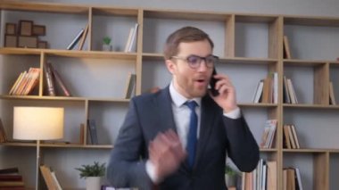Angry young business man talking on the mobile phone while standing in the middle of the office. Busy work of a bank employee, loan arrears. Vertical video