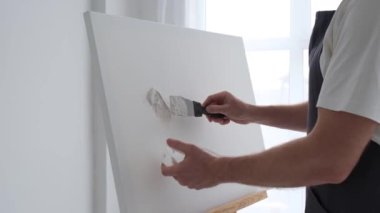 Sanatçı alçı kullanarak beyaz bir tuval üzerinde bir resim yaratıyor. Bir sanatçının soyut bir resim yapma süreci. Dikey video