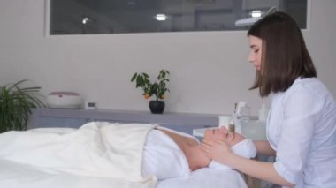 Bir kadının boynuna masaj yapan profesyonel bir masözün yan görüntüsü. Kız masaj masasına uzanıp rahatlıyor.. 