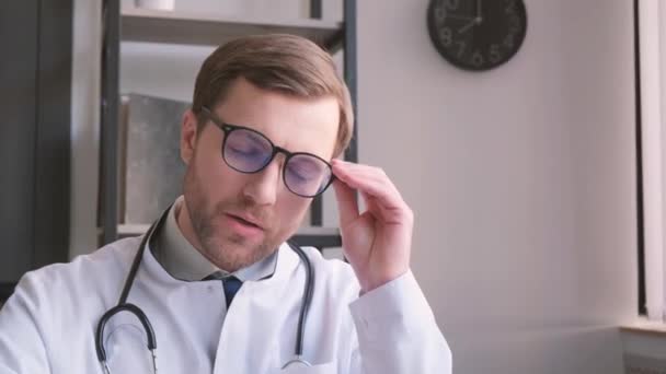 Κουρασμένος Λυπημένος Γενειοφόρος Γιατρός Λευκό Παλτό Απογειώνεται Γυαλιά Κάθεται Στο — Αρχείο Βίντεο