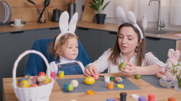 幸せな母親と娘はキッチンルームでイースターエッグを描きます 家族はイースター休暇の準備をしています イースターのウサギの耳のかわいい女の子 4Kビデオ — ストック動画
