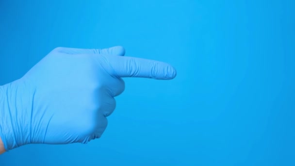 青い背景に青い医療用手袋の手のイメージ 人差し指の手は何かまたは誰かを指す 人間の手のジェスチャー — ストック動画