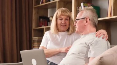 Birbirine aşık gülümseyen son sınıf çifti bilgisayar aracılığıyla koltukta otururken görüntülü bir konuşma yapıyorlar. Büyükbabalar ve modern teknolojiler