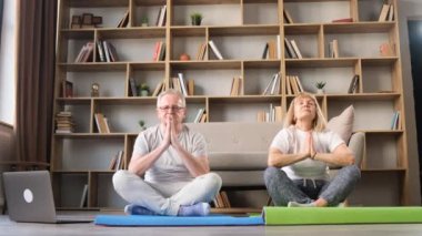 Son sınıf çifti oturma odasında arka planda kitaplarla jimnastik minderleri üzerinde yoga yapıyor. Kendinle uyum içinde. Sağlık için meditasyon