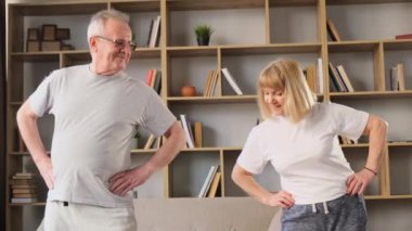 Yaşlı çiftin sabah jimnastiği. Kadın ve erkek oturma odasında bel egzersizi yapıyor. Yaşlılar için taşınabilir yaşam tarzı kavramı.