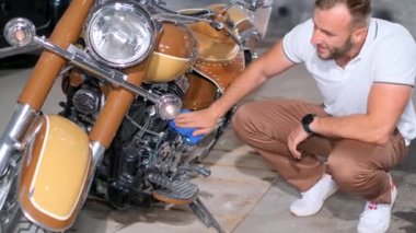 Motosikletin yanındaki garajda genç bir adam krom motoru parlayana kadar ovuyor. Güzel bir retro motosiklet. Dikey video