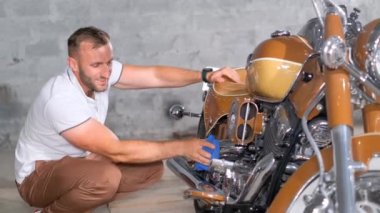 Bir adam bir garajda motosikletinin krom parçalarını temizler ve parlatır. Motosikletini sev