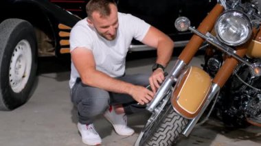 Sakallı bir adam yola çıkmadan önce motosikletinin frenlerini kontrol eder. Garajda bir motosikletin teşhisi. Hobi motorcusu. Dikey video