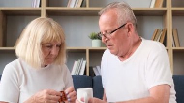 Grandfather takes care of grandmother, her heart hurts. Pensioners are sitting at home on the couch and being treated for hypertension