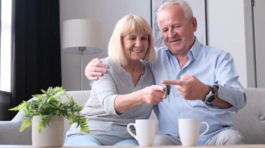 The elderly couple together hold the keys to the bought new house. Happy American retirees. Fulfilling a dream in old age