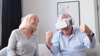 An older man drives a car wearing virtual glasses and his wife laughs at him. Happy modern retirees.
