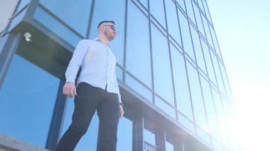 A young office manager stands near a skyscraper and looks ahead. Businessman outdoors.