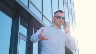 An evil boss is talking on the phone near a skyscraper. Successful stylish businessman on the street near the office center.