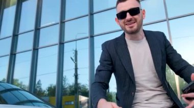 Confident business man talking to the camera while waving his hands against the background of an office center. Handsome young manager