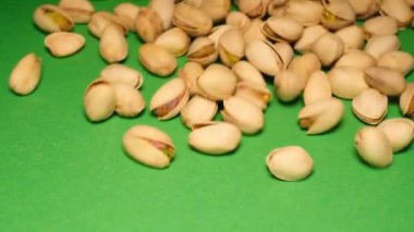 Pistachios fall on a green background in slow motion.