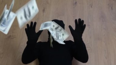 A robber in a black mask tosses dollars. A successful bank robbery.