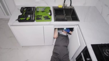 A plumber installing a sink in the kitchen room. Repair work in a new building.