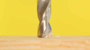 Super slow motion of drilling holes in wood with a drill. The drill rotates on a yellow background.