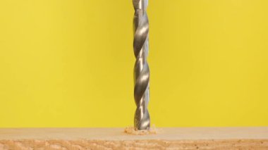 Close-up of drilling holes in wood with a drill. The drill rotates on a yellow background.